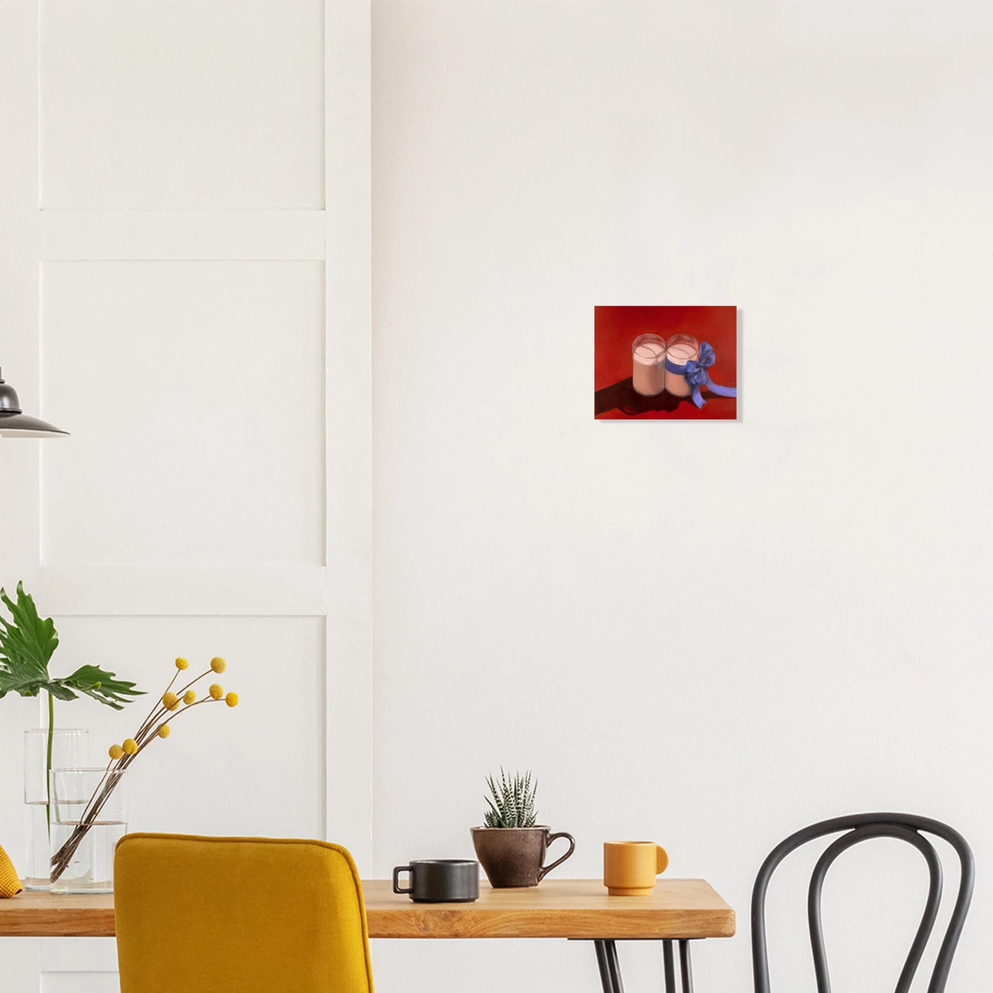 Jay Didyk's "Happy Holidays!" painting against a white wall. Wooden dining table with various mugs and potted plants, and two chairs at the bottom quadrant of the photo.