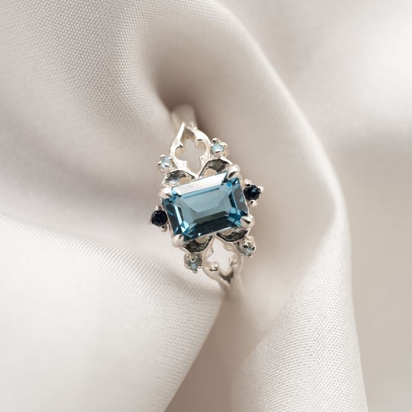 Silver gothic ring with a blue gemstone on white fabric