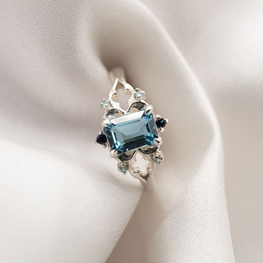 Silver gothic ring with a blue gemstone on white fabric